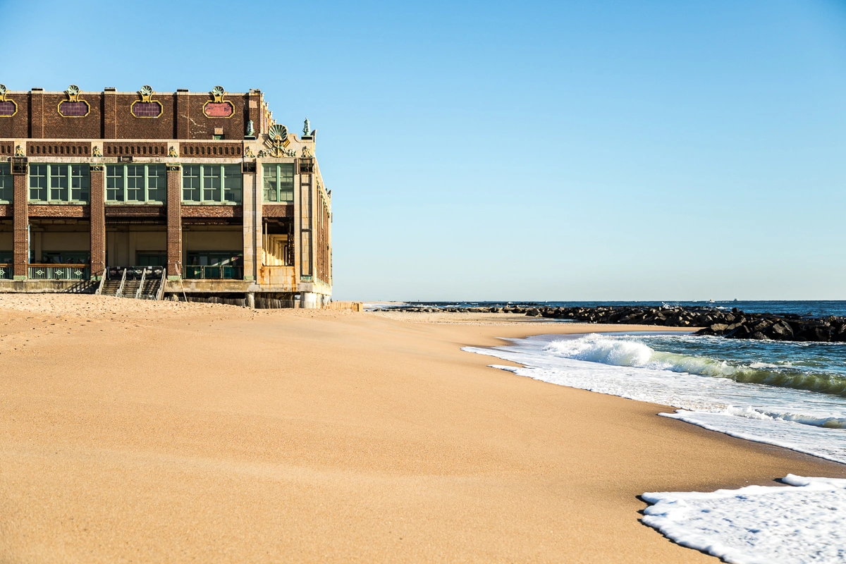 Historic Paramount Theatre and Convention Hall in Asbury Park, NJ, with white-capped waves and the Atlantic Ocean shoreline.